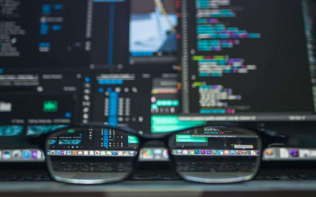 Fotografia de unas gafas mediante las cuáles vemos de manera enfocada el código de programación en un monitor